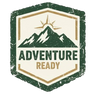 A distressed vintage-style shield logo featuring a mountain graphic and the words 'ADVENTURE READY' in dark green and tan on a cream background, centered on a plain white backdrop.